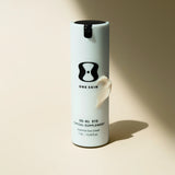 White cylindrical container with black lid labeled 'One Skin' on a beige background